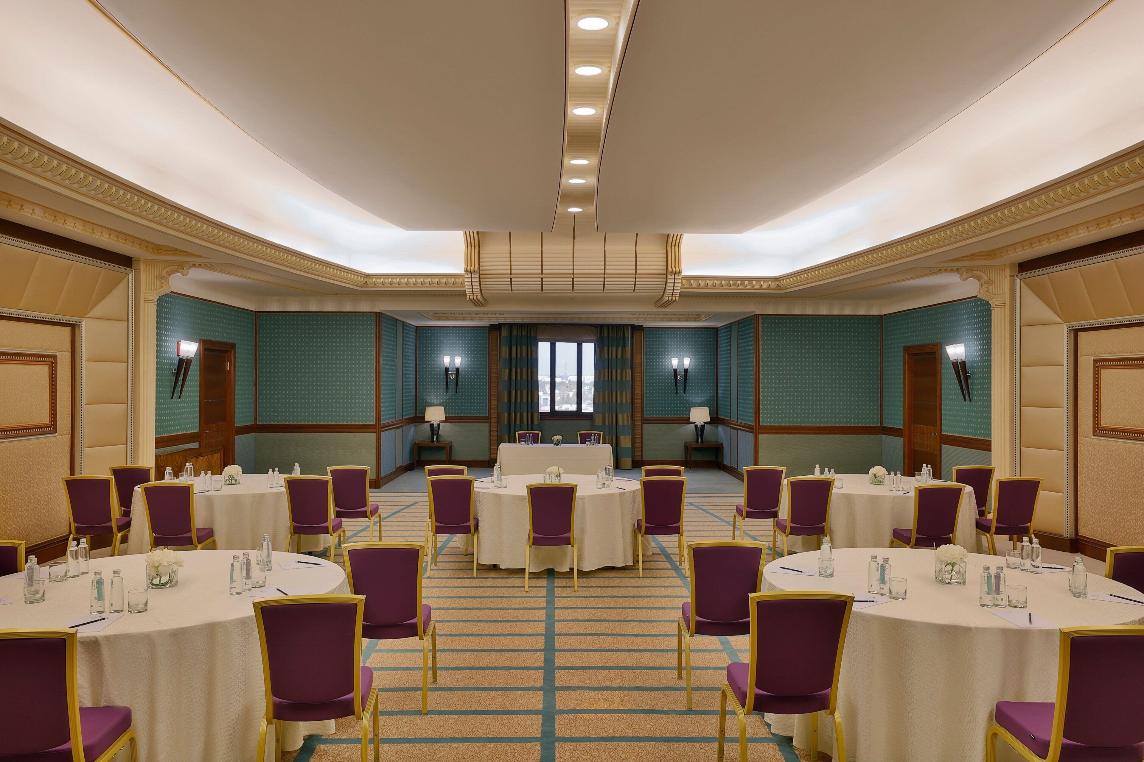 A conference room with multiple round tables, purple chairs, and a carpeted floor.