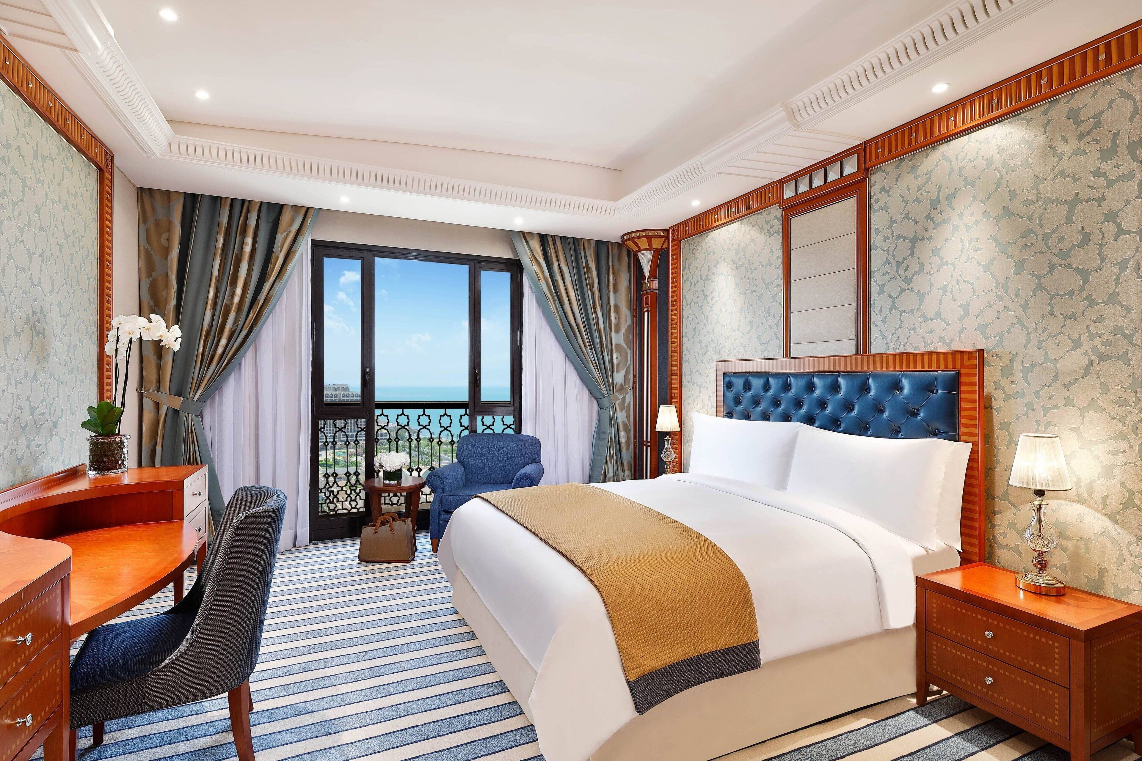 A hotel room with a large bed, a desk, a chair, a nightstand, and a view of the outdoors.