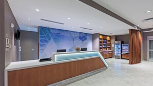 Un espace d’accueil comprenant un comptoir de réception en bois, un panneau d’information bleu, un distributeur automatique et un réfrigérateur.