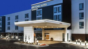 Une entrée d’hôtel moderne avec une allée couverte, de grandes fenêtres et une enseigne indiquant « SPRINGHILL SUITES MARRIOTT ».