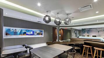 A modern hotel lobby with a 'Stay' advertisement, a reception desk, and a bar area.