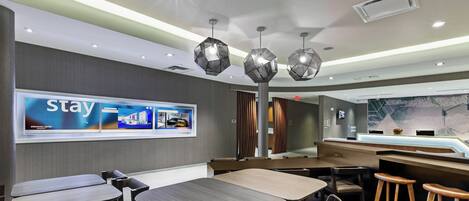 A modern hotel lobby with a 'Stay' advertisement, a reception desk, and a bar area.