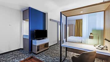 Habitación de hotel con escritorio, televisión, cama, espejo y una pequeña mesa.