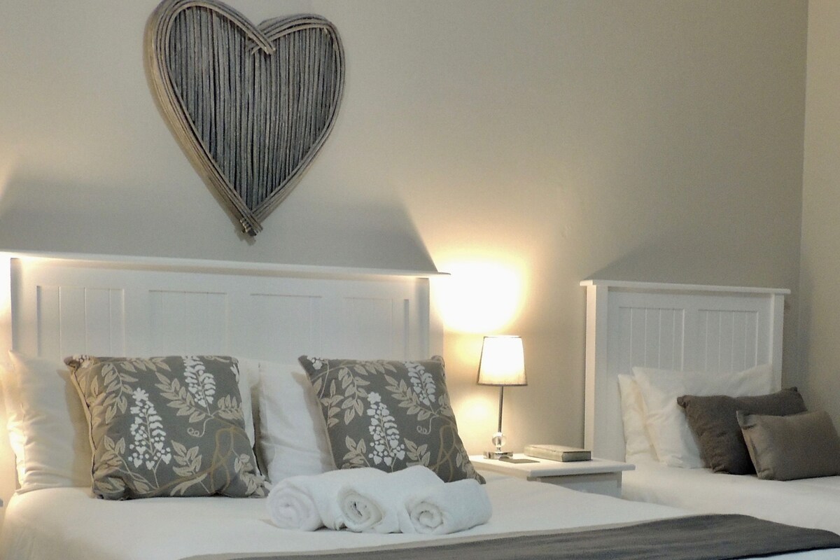 A neatly made bed with floral pillows, a heart-shaped wall decoration, and a bedside lamp.