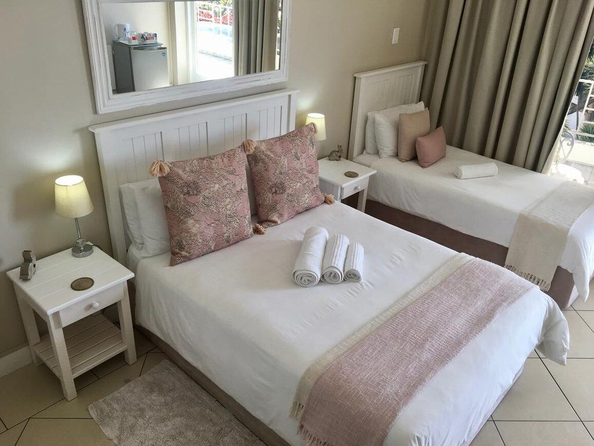 Habitación de hotel con dos camas, cada una con cabecero blanco, mesita de noche con lámpara y espejo sobre el cabecero.