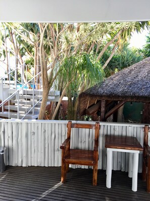 A wooden deck with two wooden chairs and a small table, surrounded by a white fence and tropical plants. - La Mer Guesthouse (Gqeberha (Port Elizabeth))