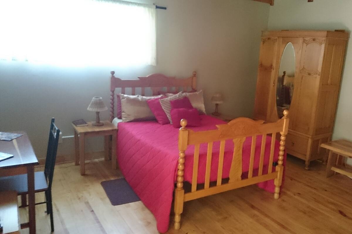 A bedroom with a wooden bed, a wardrobe, a desk, and a chair.