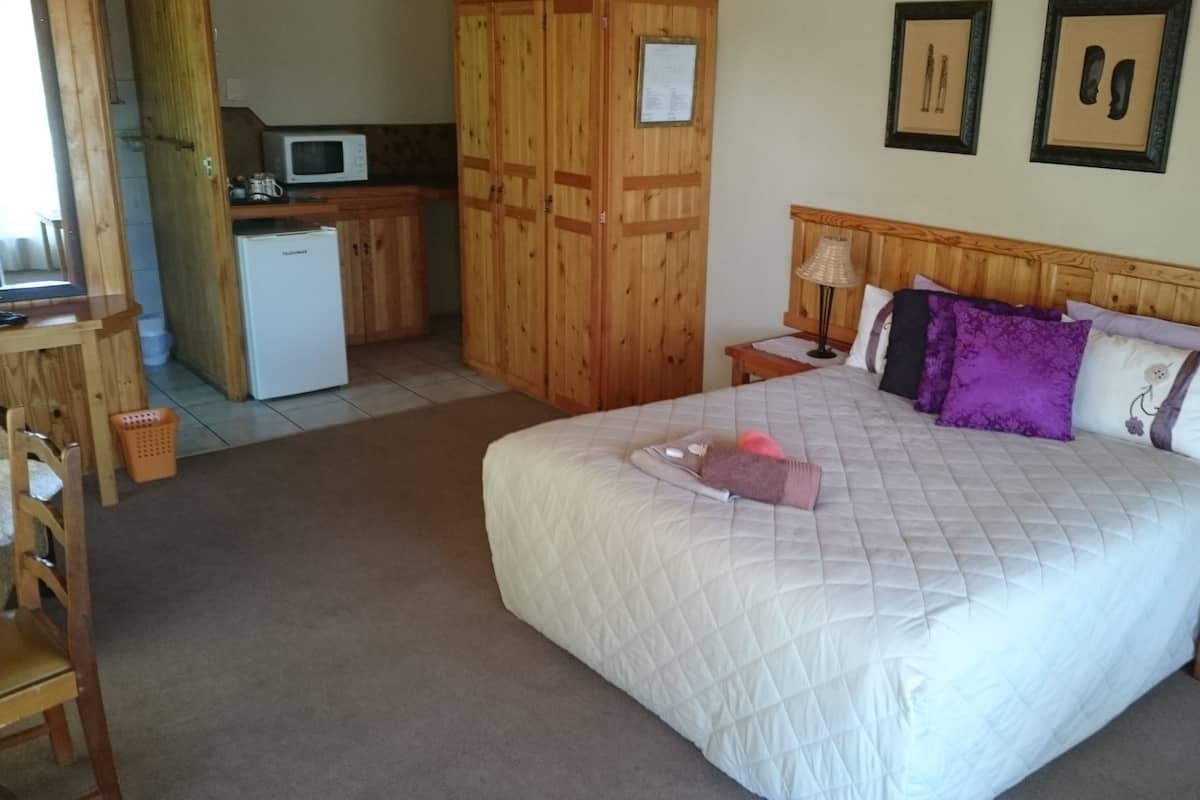 A bedroom with a large bed, wooden wardrobe, a small kitchenette, and framed pictures on the wall.