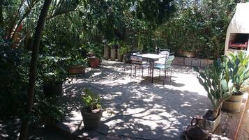 A patio area with a table and chairs, surrounded by potted plants and trees.