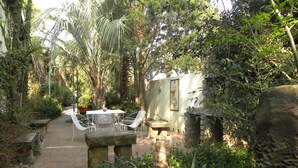 A garden with a stone bench, a table with chairs, and a pathway. - Ladybrand Guest House (Mantsopa)