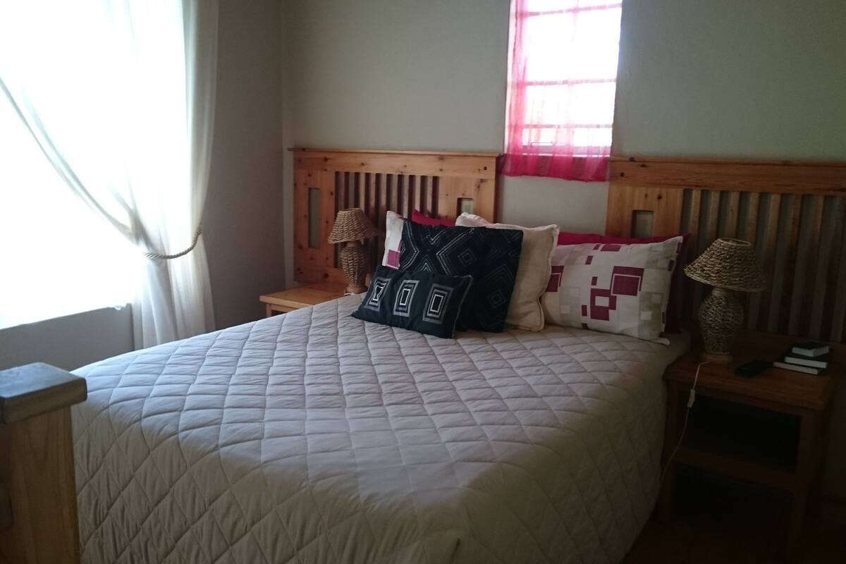A bed with a quilted bedspread, two bedside lamps, and a window with curtains.