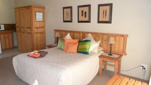 A bedroom with a large bed, wooden headboard, multiple pillows, a nightstand with a lamp, and a wooden wardrobe. - Ladybrand Guest House (Mantsopa)
