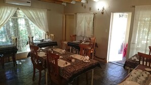 A dining area with zebra-patterned tablecloths, wooden chairs, and a view of the outdoors through large windows. - Ladybrand Guest House (Mantsopa)