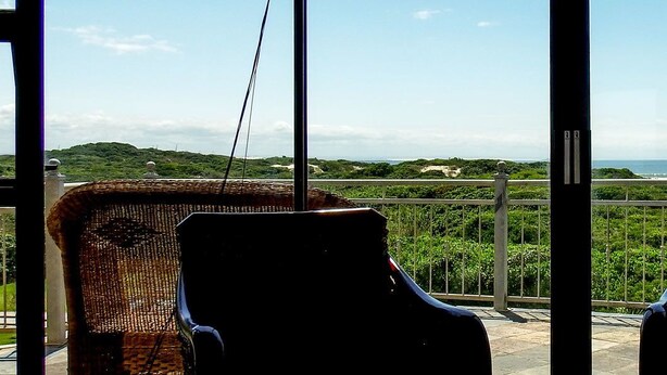 Two wicker chairs facing a balcony with a view of the sea and greenery. - House Haven Guesthouse (Gqeberha (Port Elizabeth))