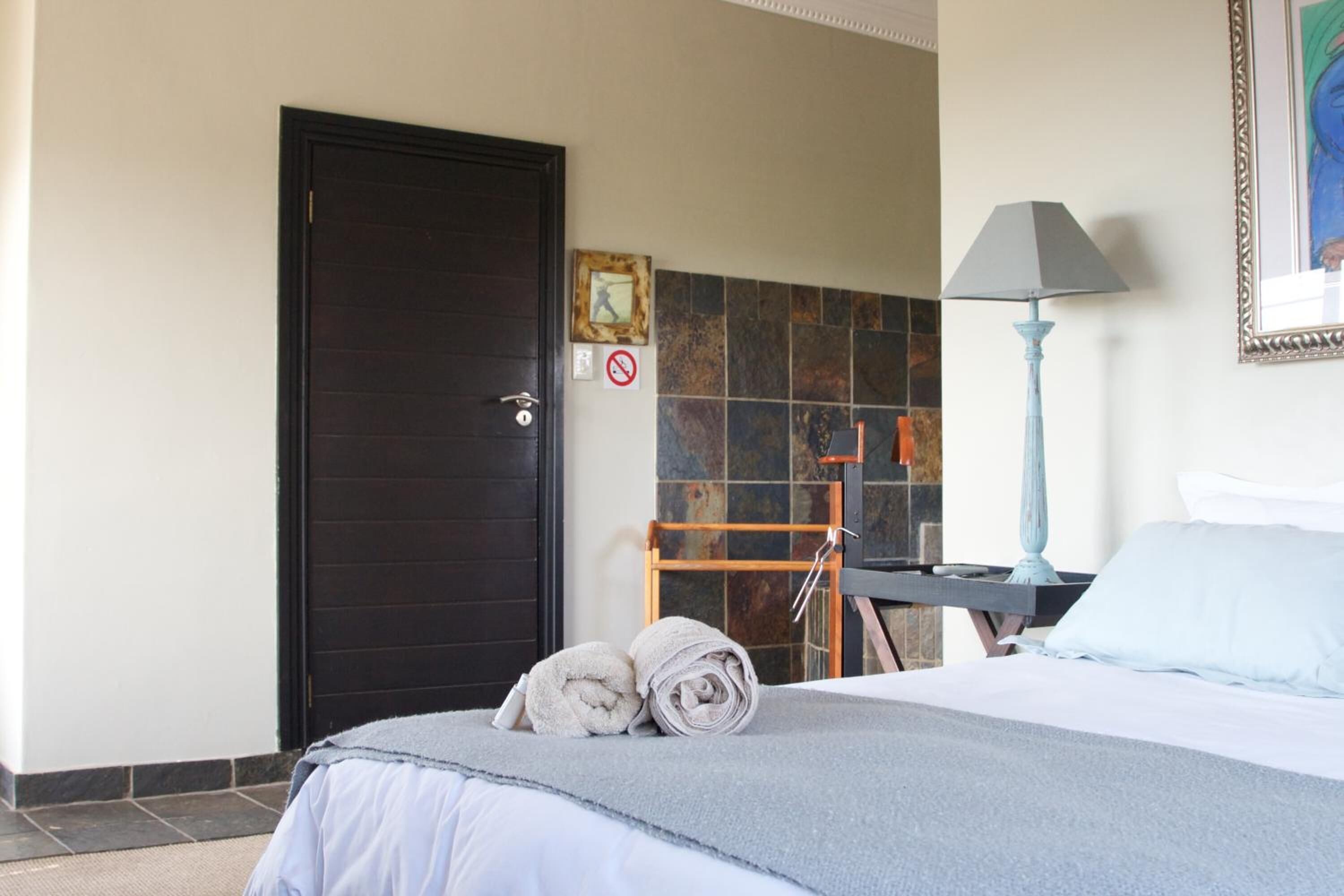 A hotel room with a bed, a towel rack, a lamp, and a door.