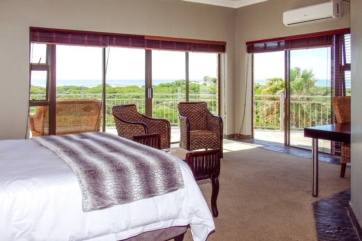 Ein Hotelzimmer mit einem großen Bett, zwei Korbstühlen, einem kleinen Tisch und einem Balkon mit Meerblick.