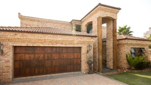 A brick house with a large garage door, a small tower-like structure, and a well-maintained lawn. - House Haven Guesthouse (Gqeberha (Port Elizabeth))