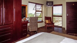 A hotel room with a bed, a chair, a desk, a television, and a balcony with a view. - House Haven Guesthouse (Gqeberha (Port Elizabeth))