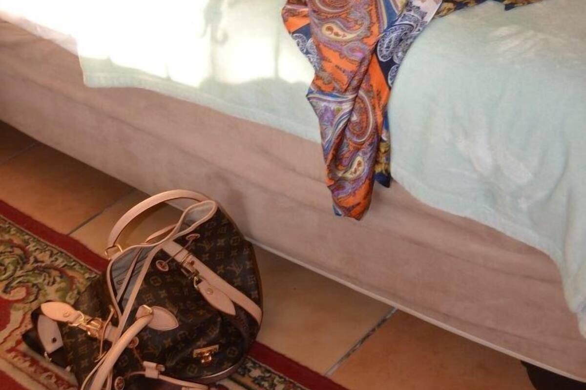 A bed with a patterned blanket, a hat, and a rolled-up scarf on it.