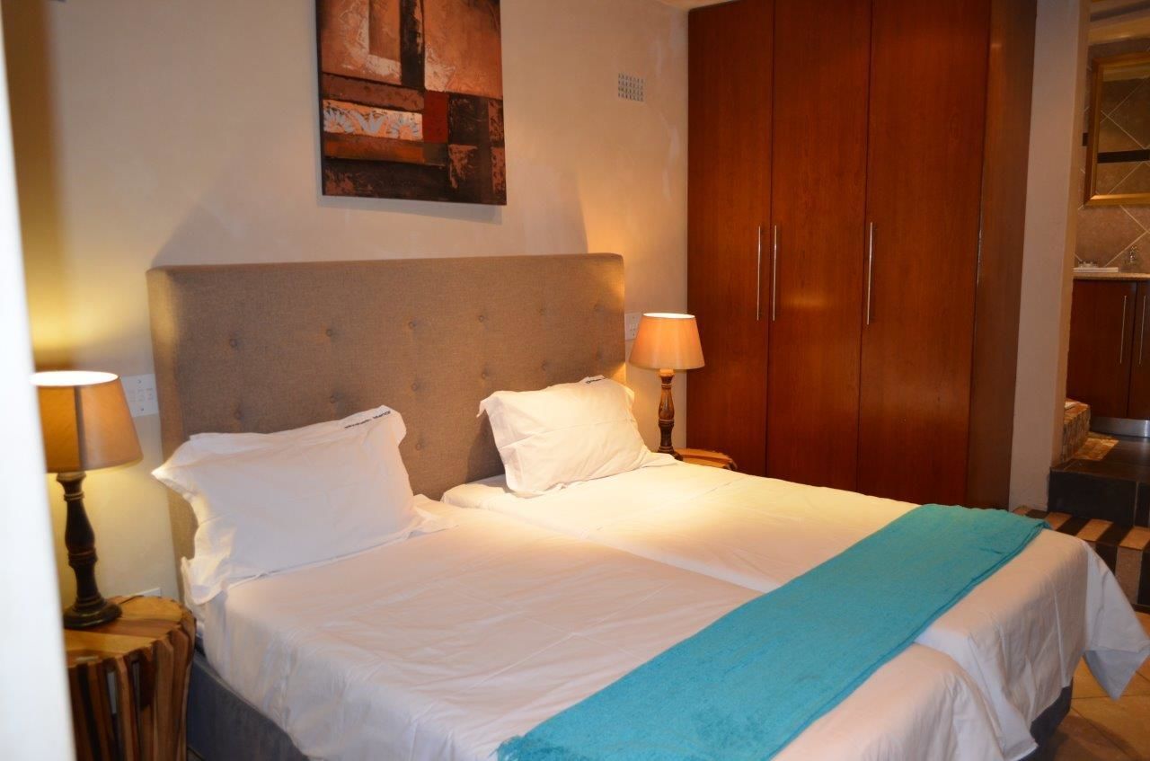 A hotel room with a large bed, wooden wardrobe, and a painting on the wall.