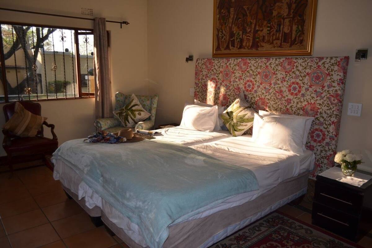 A bedroom with a bed, a chair, a nightstand, a window with curtains, and a floral-patterned headboard.