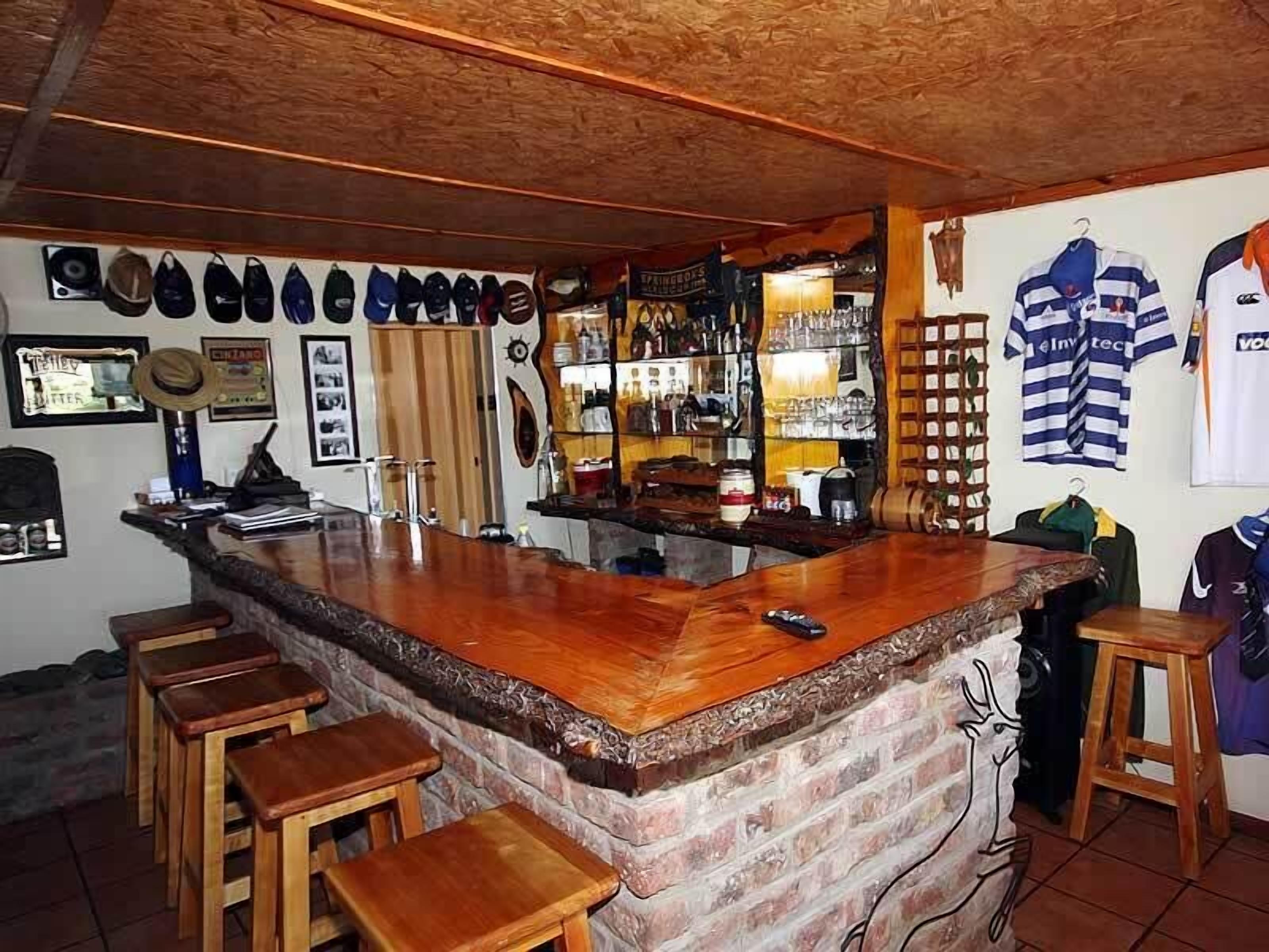 A bar area with a wooden bar counter, stools, and various items on the shelves.