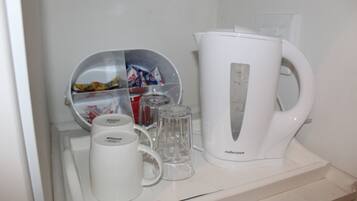 Una kitchenette con un hervidor blanco, una jarra de vidrio, una taza y un recipiente con snacks.