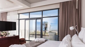 Una habitación de hotel con un ventanal grande, una cama, un televisor, un aparador de madera y una silla.