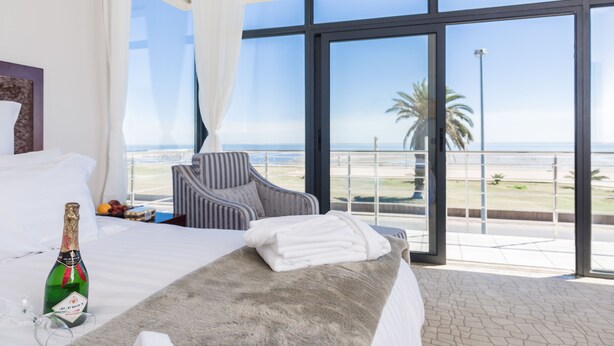 Habitación de hotel con una cama grande, una botella de champán y vistas a la playa.