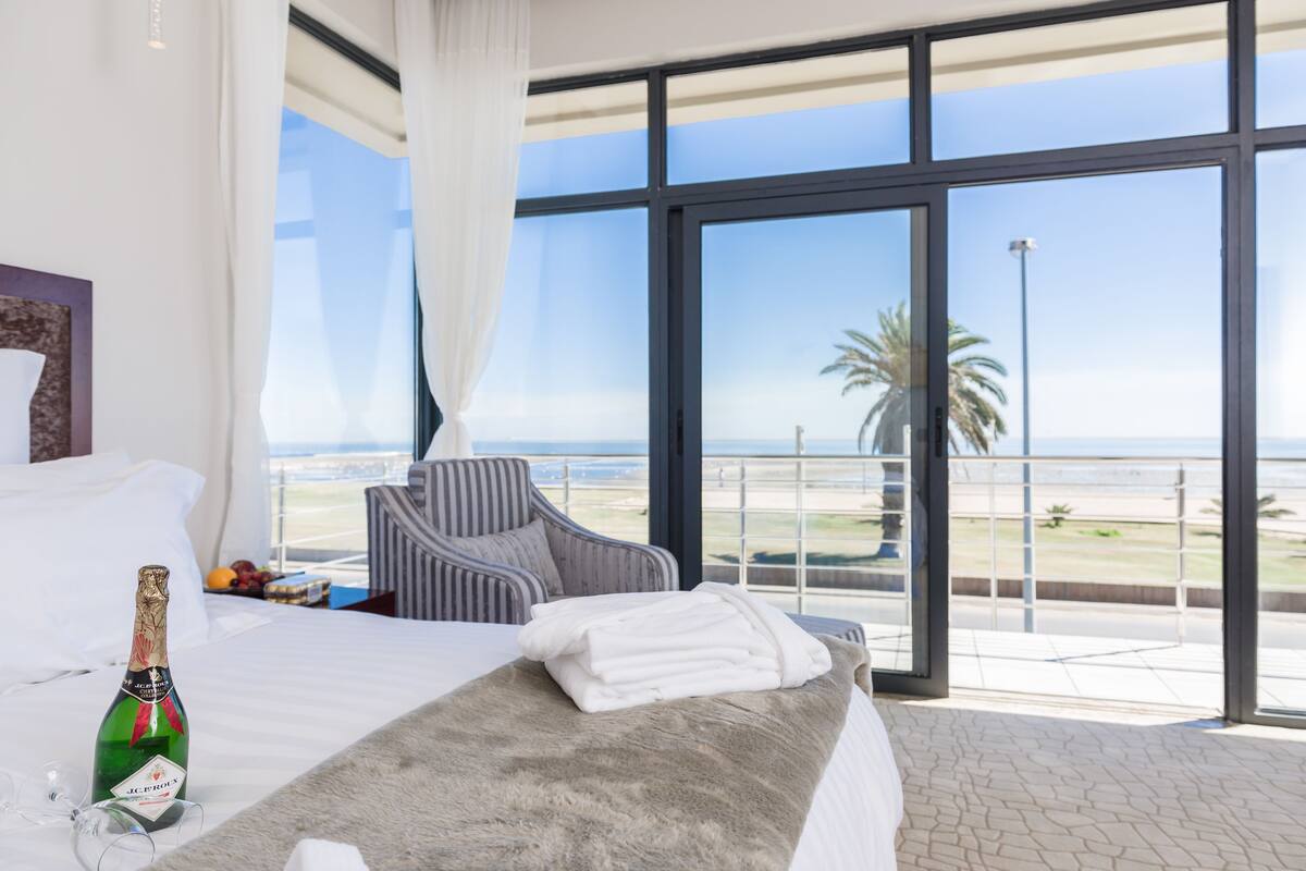 Une chambre d’hôtel avec un lit, une bouteille de champagne, une chaise et une vue sur la plage.
