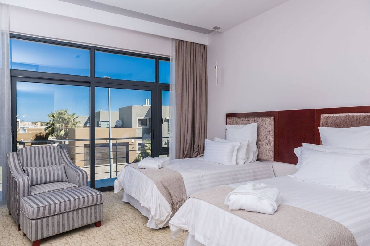 Une chambre d’hôtel avec une grande fenêtre, un lit, une chaise et une vue sur les immeubles.
