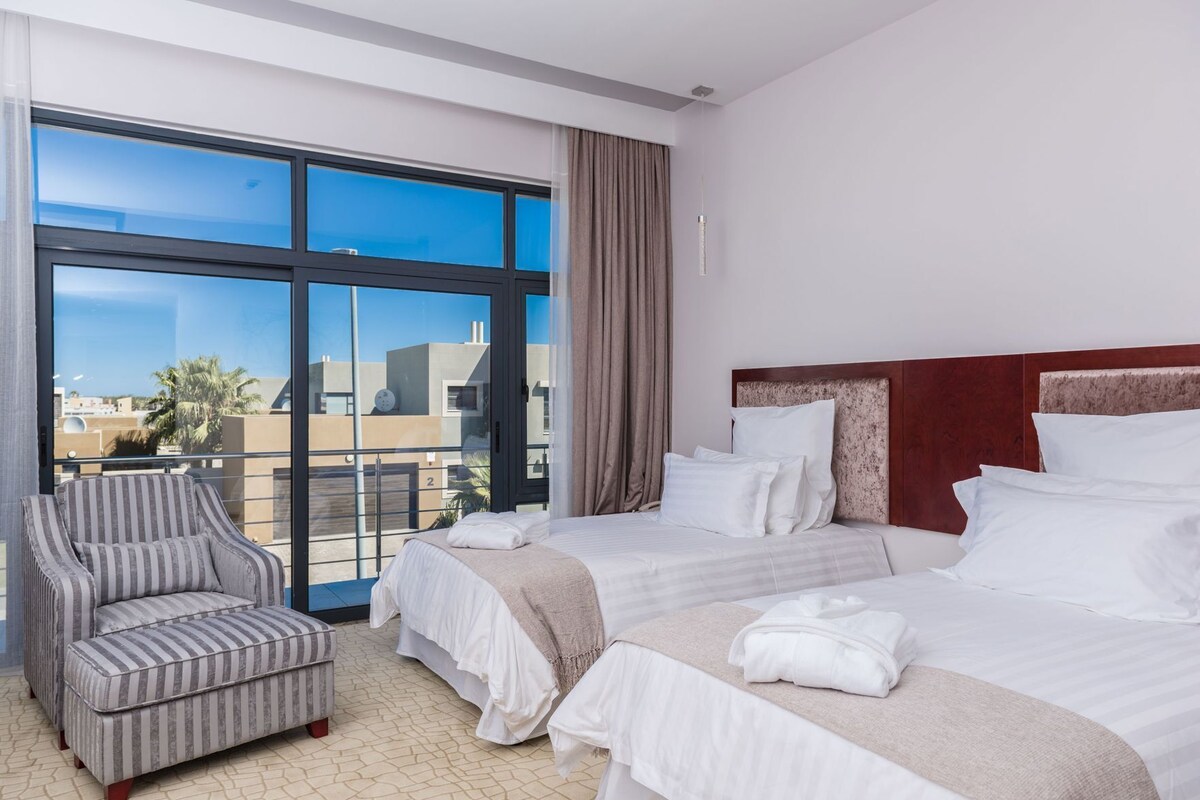A hotel room with a large window, a bed, a chair, and a view of buildings.