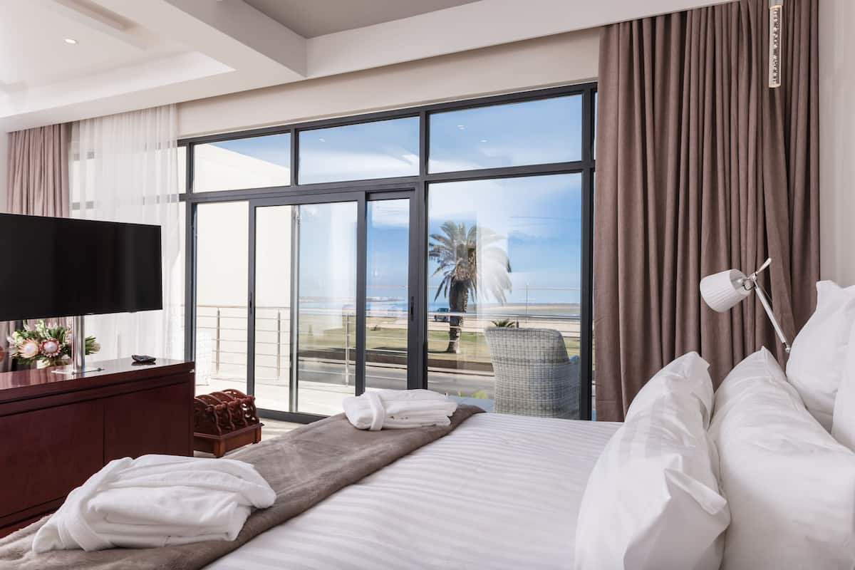 Une chambre d’hôtel avec une grande fenêtre, un lit, une télévision et une vue sur la plage.