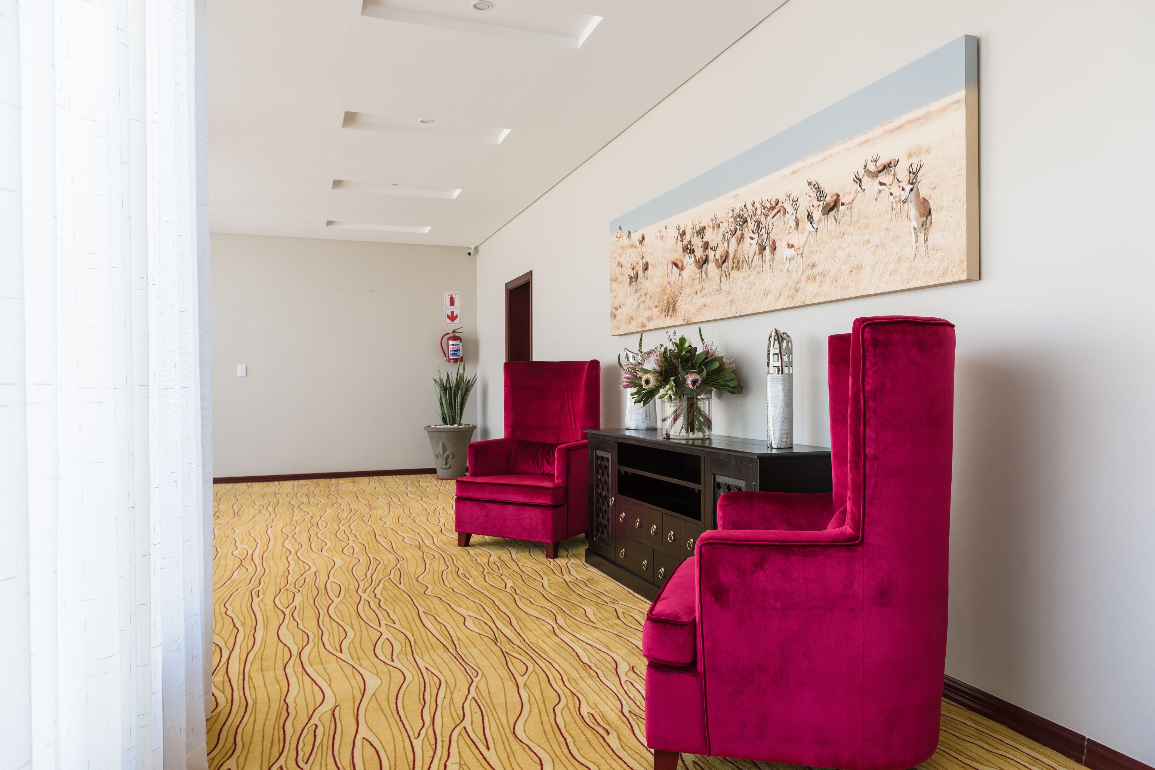 Un hall d’entrée spacieux, doté d’un tapis à motifs, d’un fauteuil rouge, d’une console en bois foncé agrémentée d’objets décoratifs et d’un grand tableau représentant des animaux sauvages accroché au mur.
