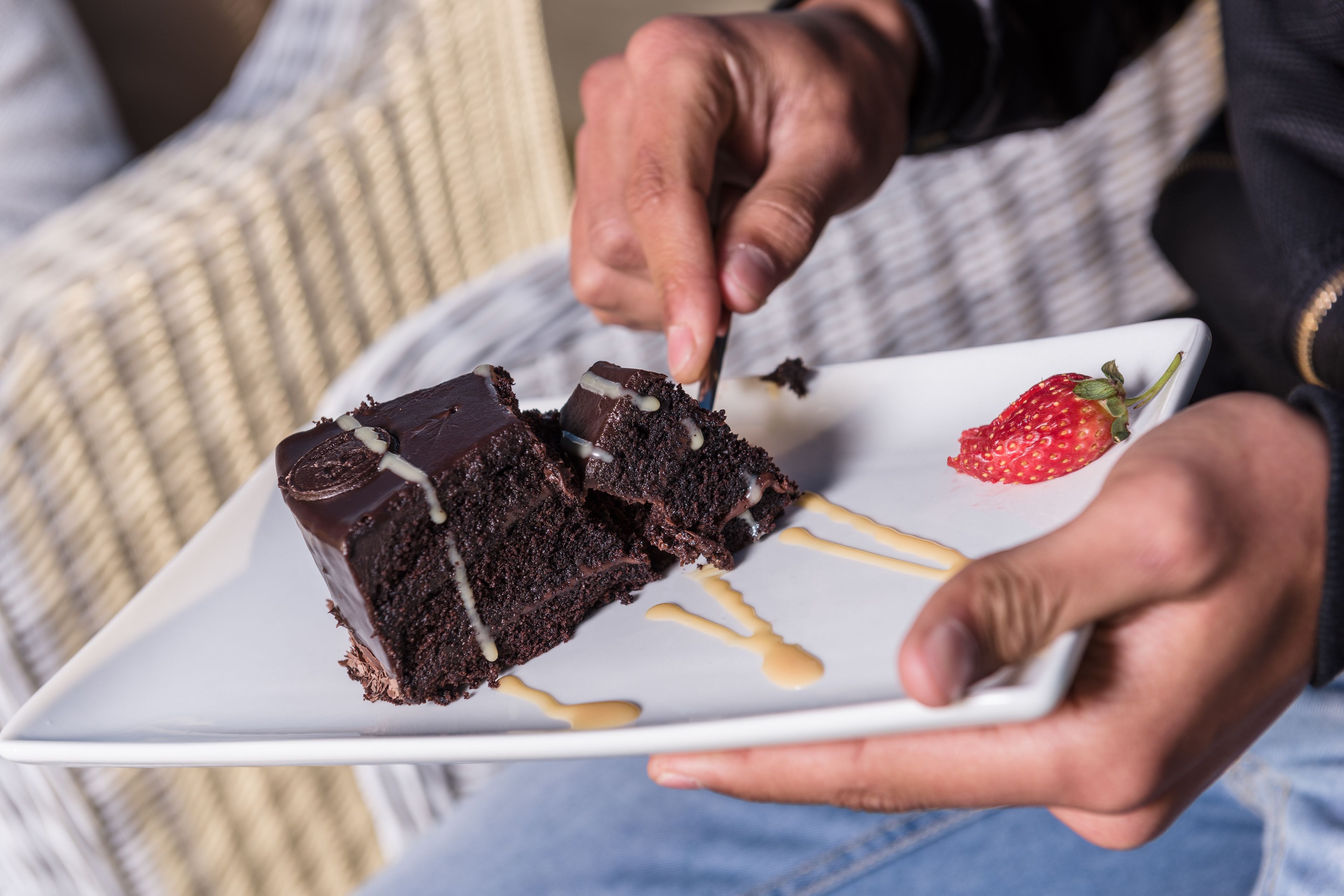Een persoon houdt een witte schaal vast met een plak chocoladecake en een aardbei.