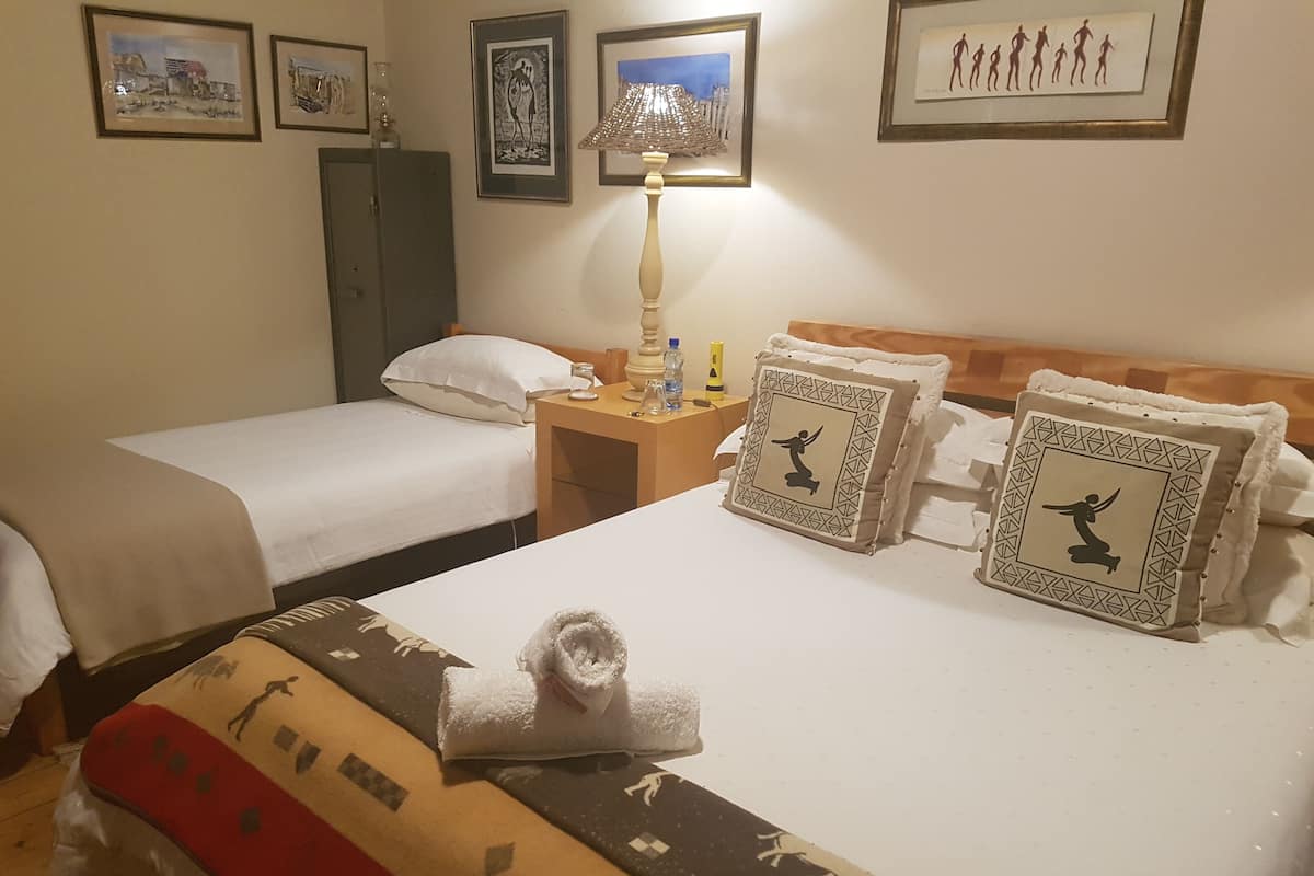 A hotel room with two single beds, a nightstand with a lamp, and decorative pillows.