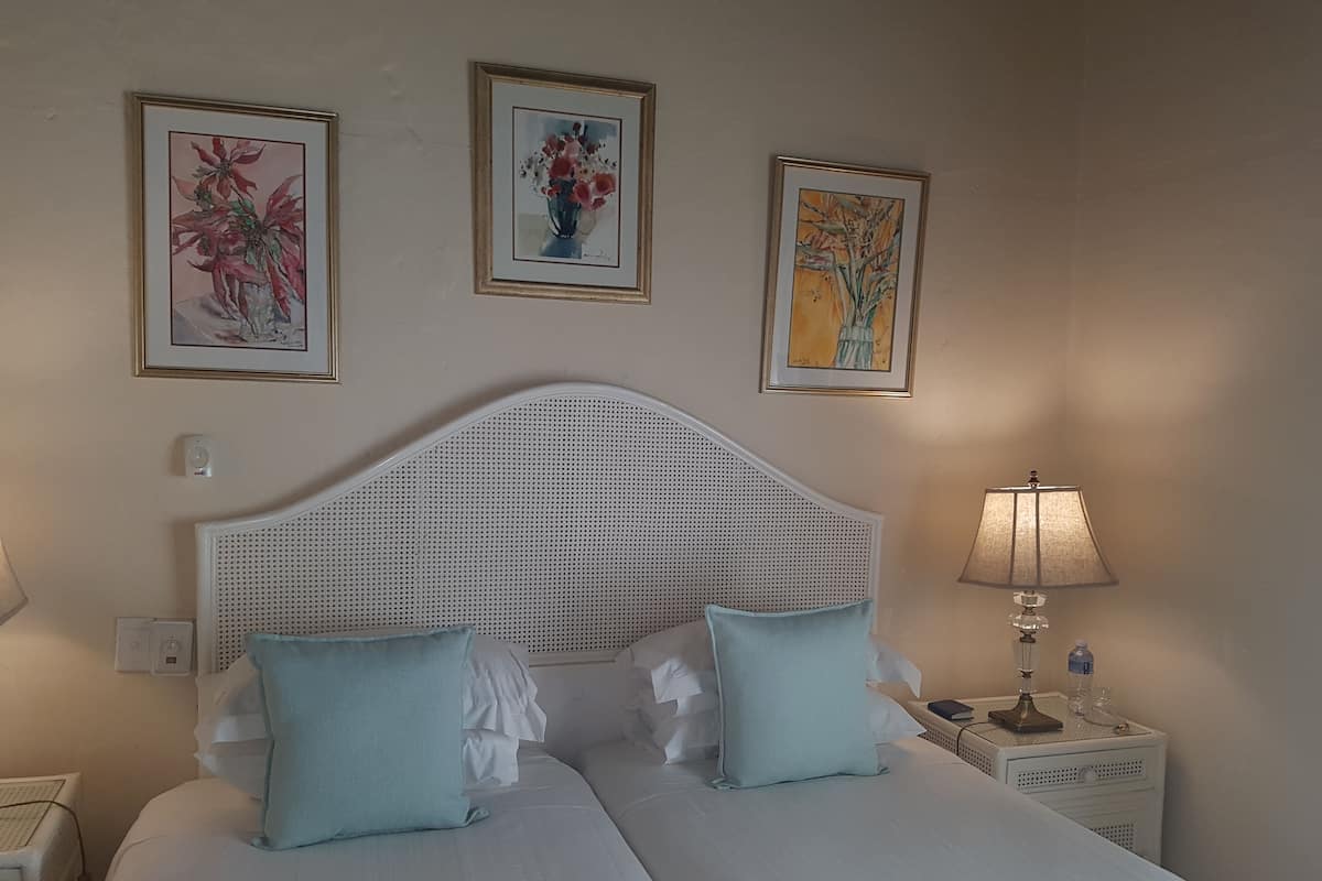 A double bed with white bedding and two light blue pillows, a white headboard, and three framed artworks on the wall.