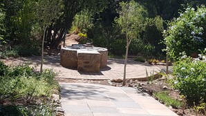 Un hogar de piedra rodeado por un camino pavimentado, con diversas plantas y árboles al fondo.