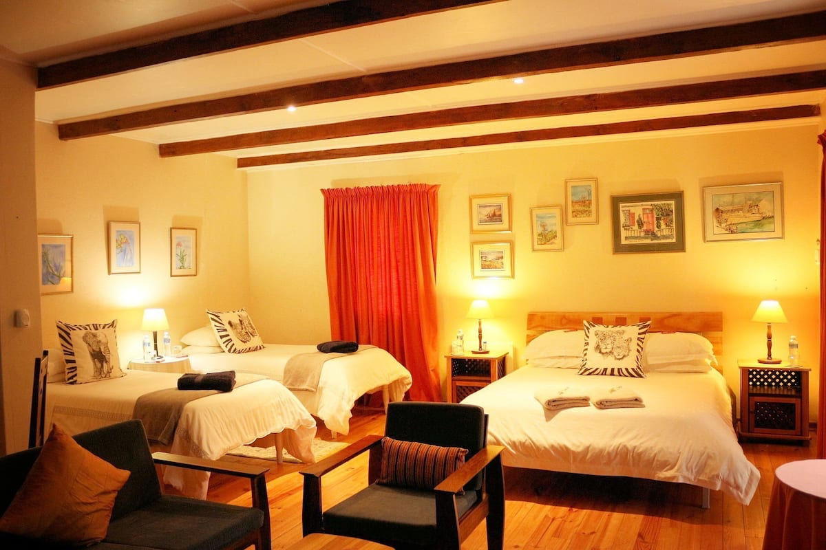 A hotel room with two beds, a wooden floor, and a red curtain. There are picture frames on the wall and a chair in the room.