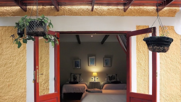 Una puerta que da a un cuarto con dos camas, una planta colgante y una lámpara.