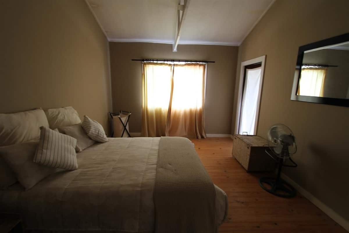 Een slaapkamer met een bed, gordijnen, een ventilator en een spiegel aan de muur.