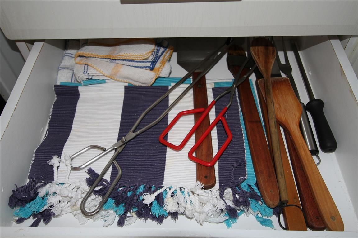 A drawer containing a striped cloth, a pair of scissors, a wooden spoon, and a metal spatula.