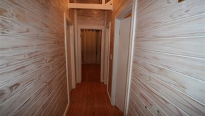 Een smalle gang met houten wanden en een houten vloer, die naar een deur aan het einde leidt.