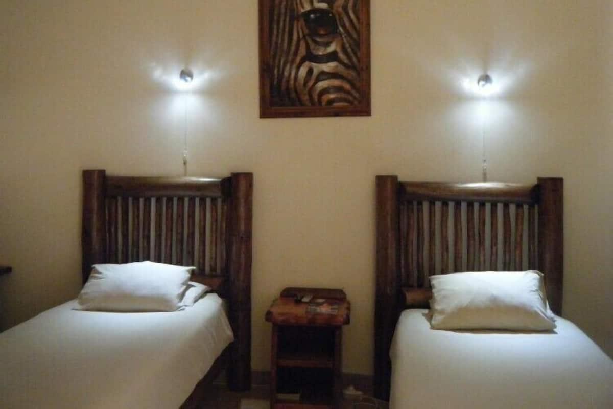 Two single beds with wooden headboards, a small table, and a zebra painting on the wall.
