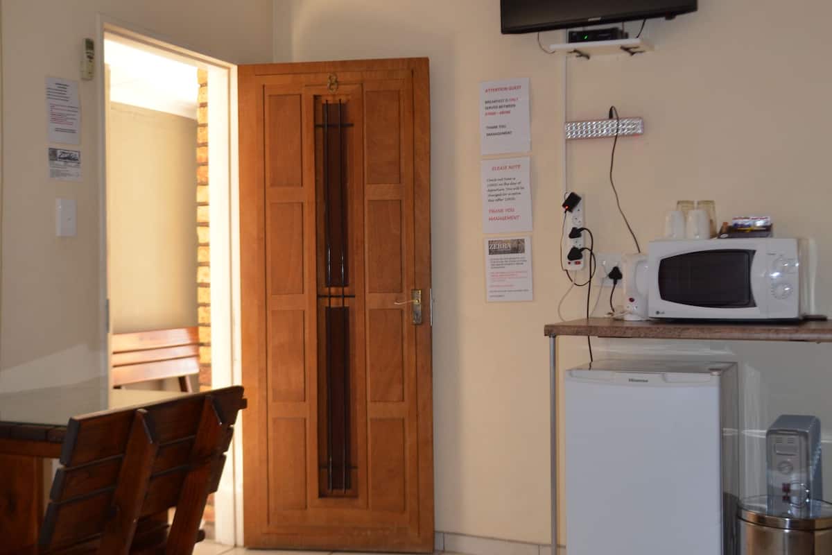 A hotel room with a bed, a desk, a microwave, a refrigerator, a trash can, a ceiling fan, a TV, and a wooden door.
