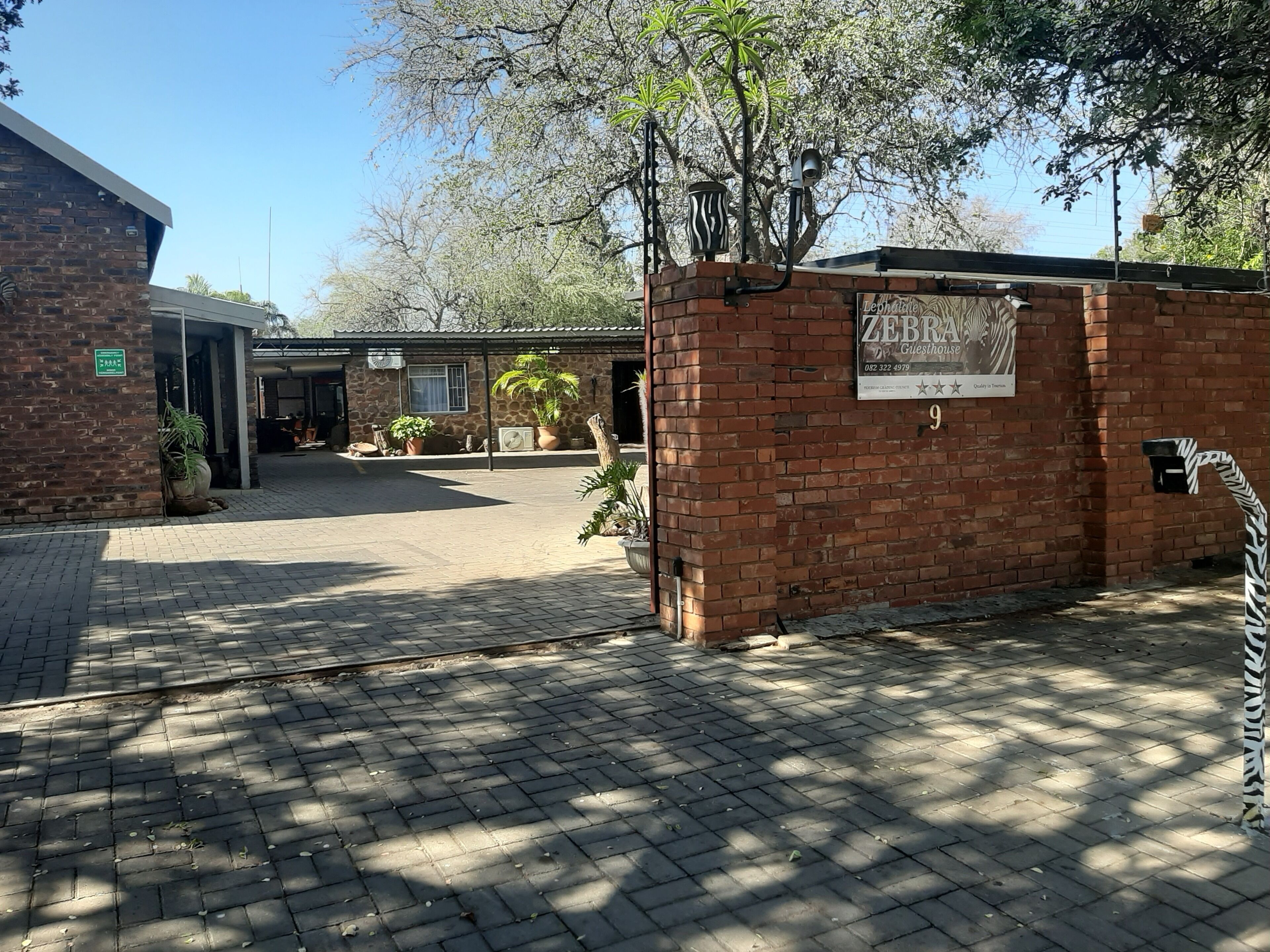 A brick building with a zebra-striped mailbox, a sign for 'Zebra Guesthouse', and a paved entrance area with potted plants.