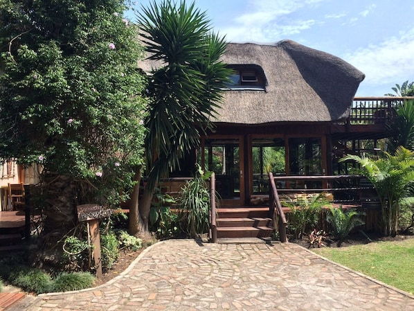 A rustic building with a thatched roof, a wooden reception desk, and a stone pathway leading to the entrance.