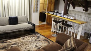 A living room with a sofa, a patterned rug, and a bar area with stools and kitchenware. - Tidewaters Accommodation (East London)