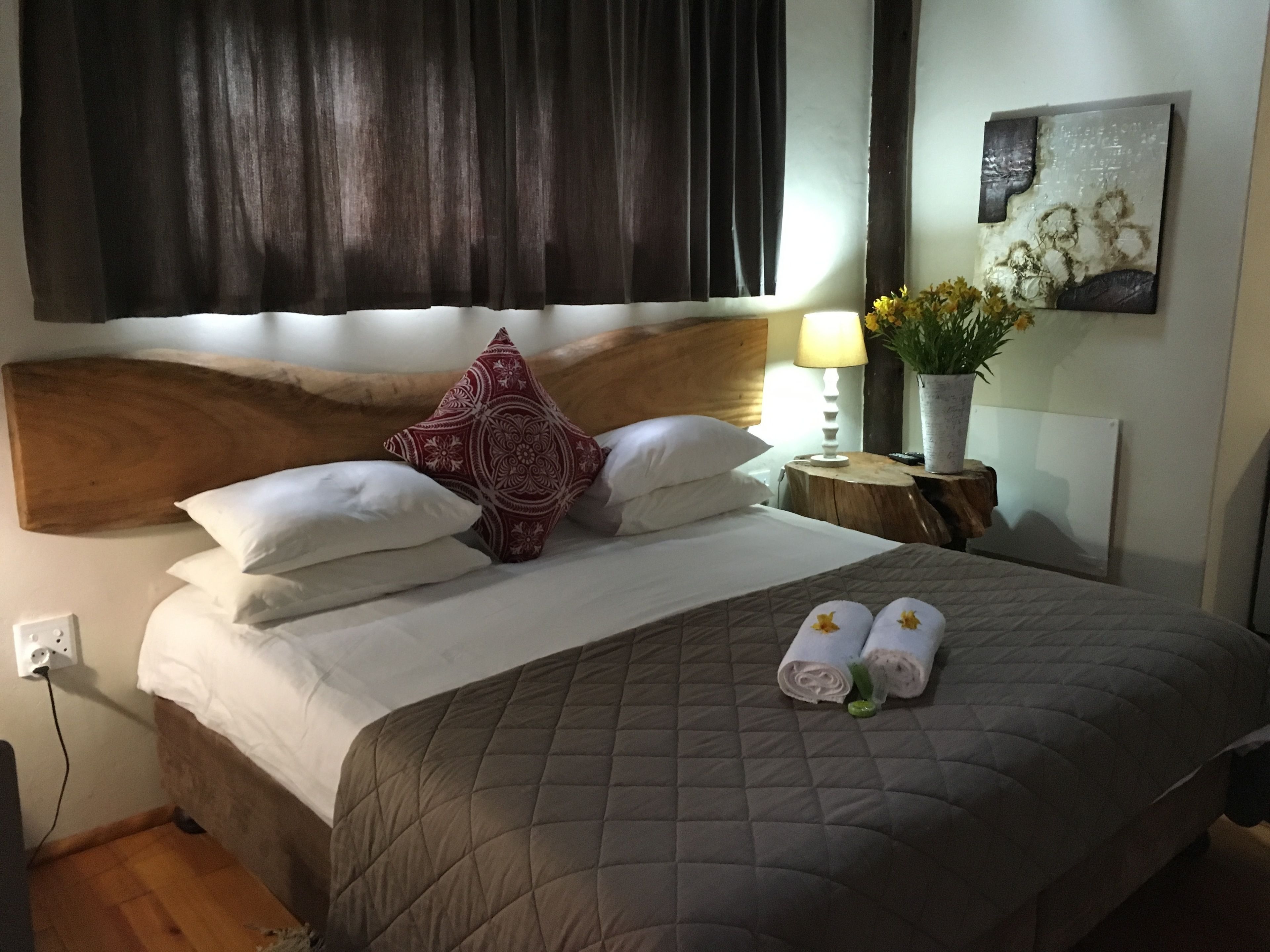 A neatly made bed with a quilted bedspread, two pillows, and two rolled towels on the bed.