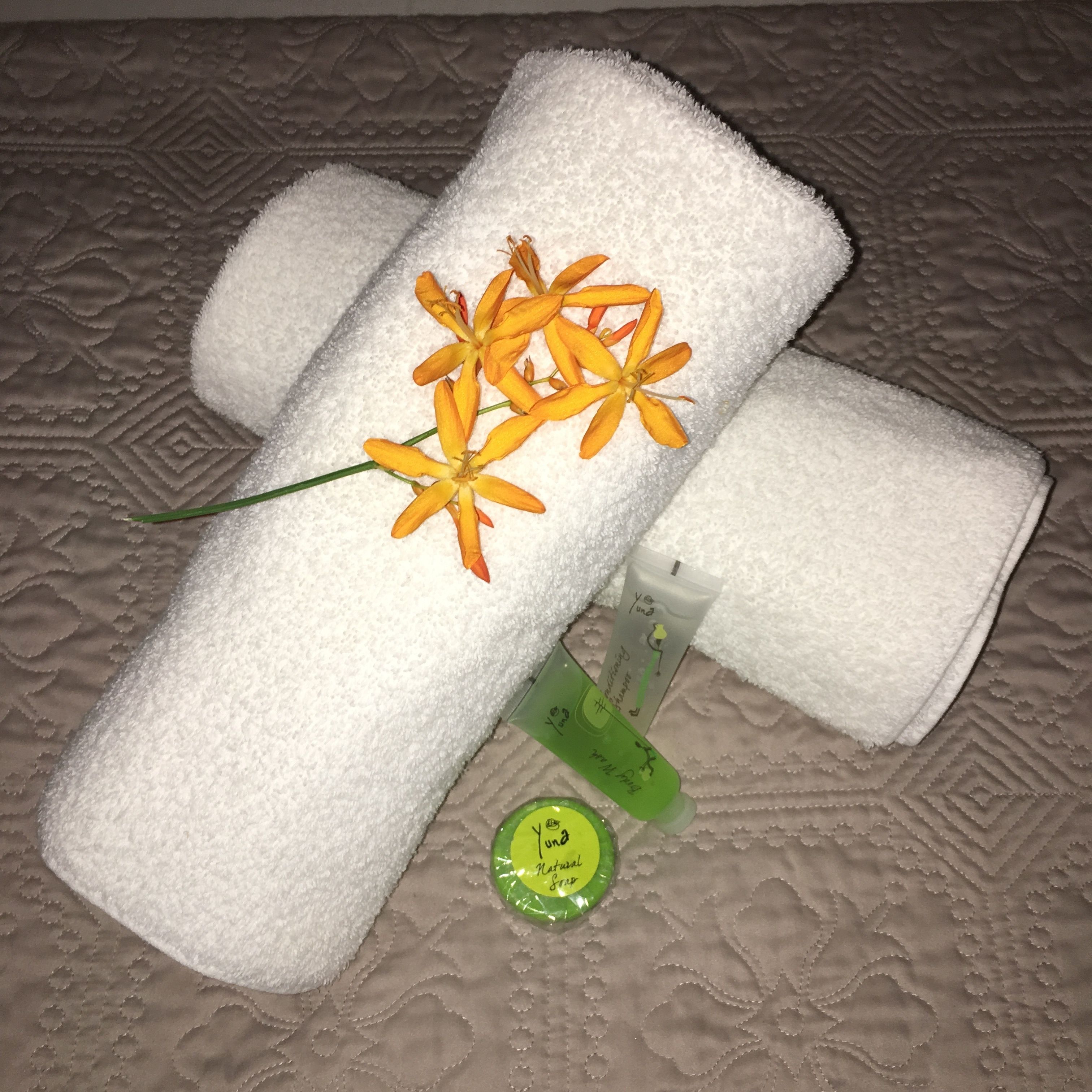 Toalha branca enrolada com uma flor amarela e uma garrafa verde sobre uma superfície texturizada.